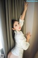 A woman in a white shirt leaning against a curtain.